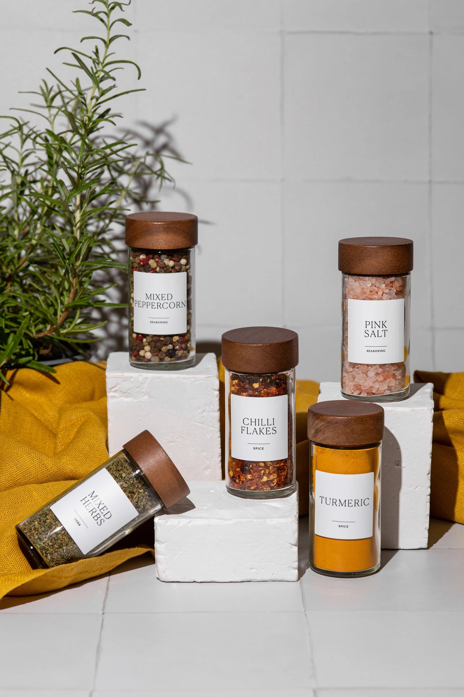 A curated set of glass spice jars filled with peppercorns, chilli flakes, pink salt and turmeric