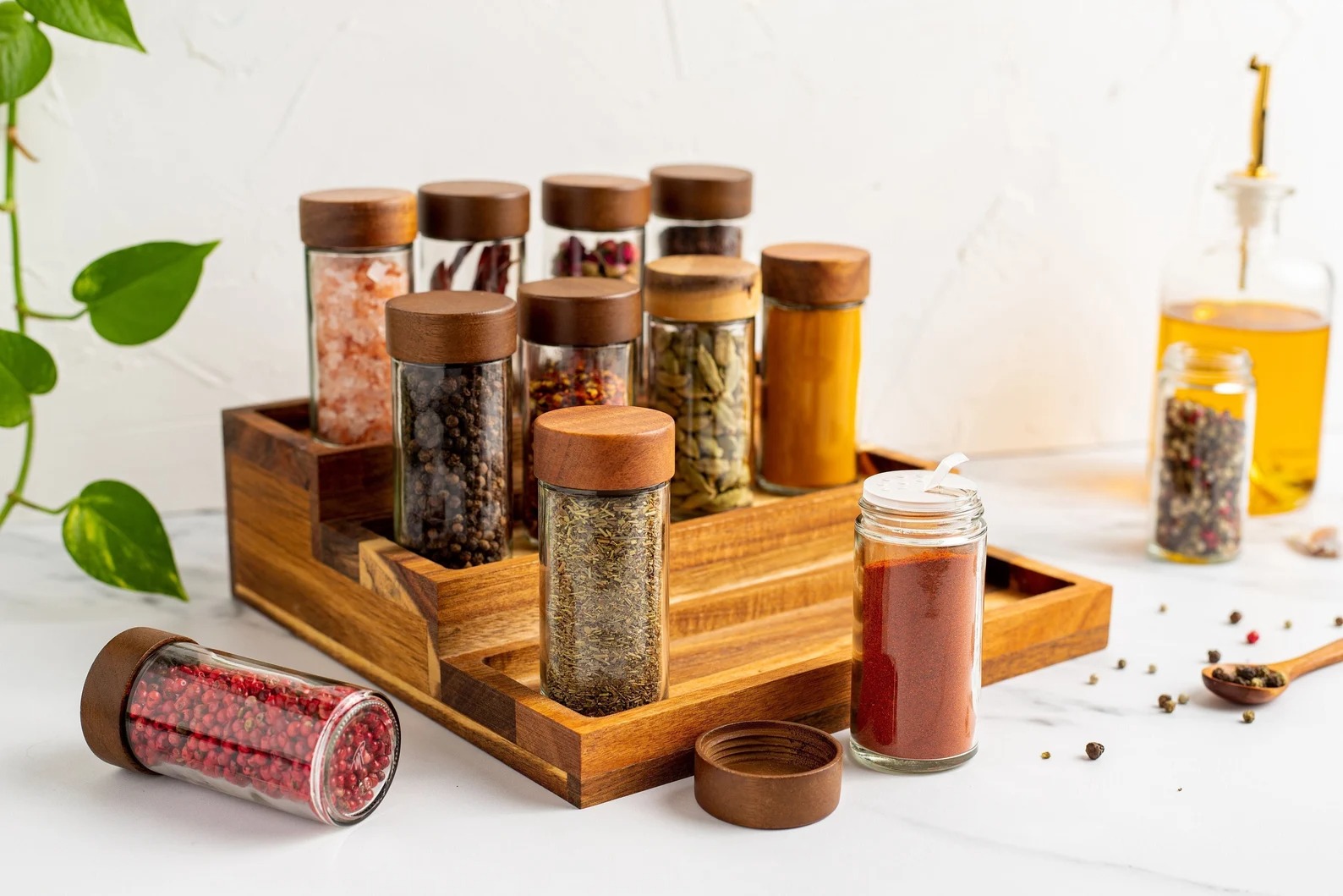Wooden spice rack holding glass jars of peppercorns, salt, chilli and herbs in a bright kitchen