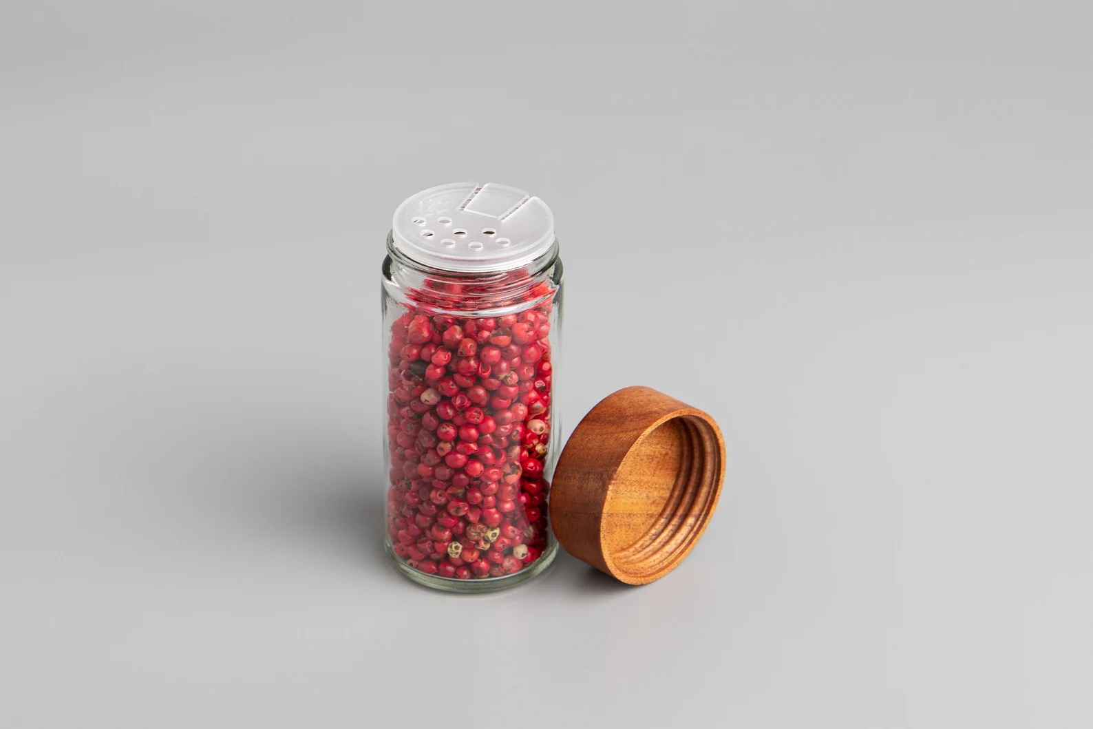 Glass shaker jar filled with bright pink peppercorns and a wooden lid